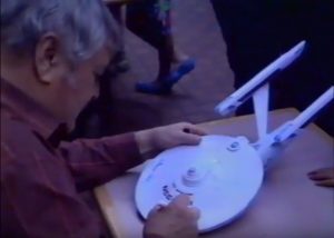 Actor James Doohan signing a model of the USS Enterprise